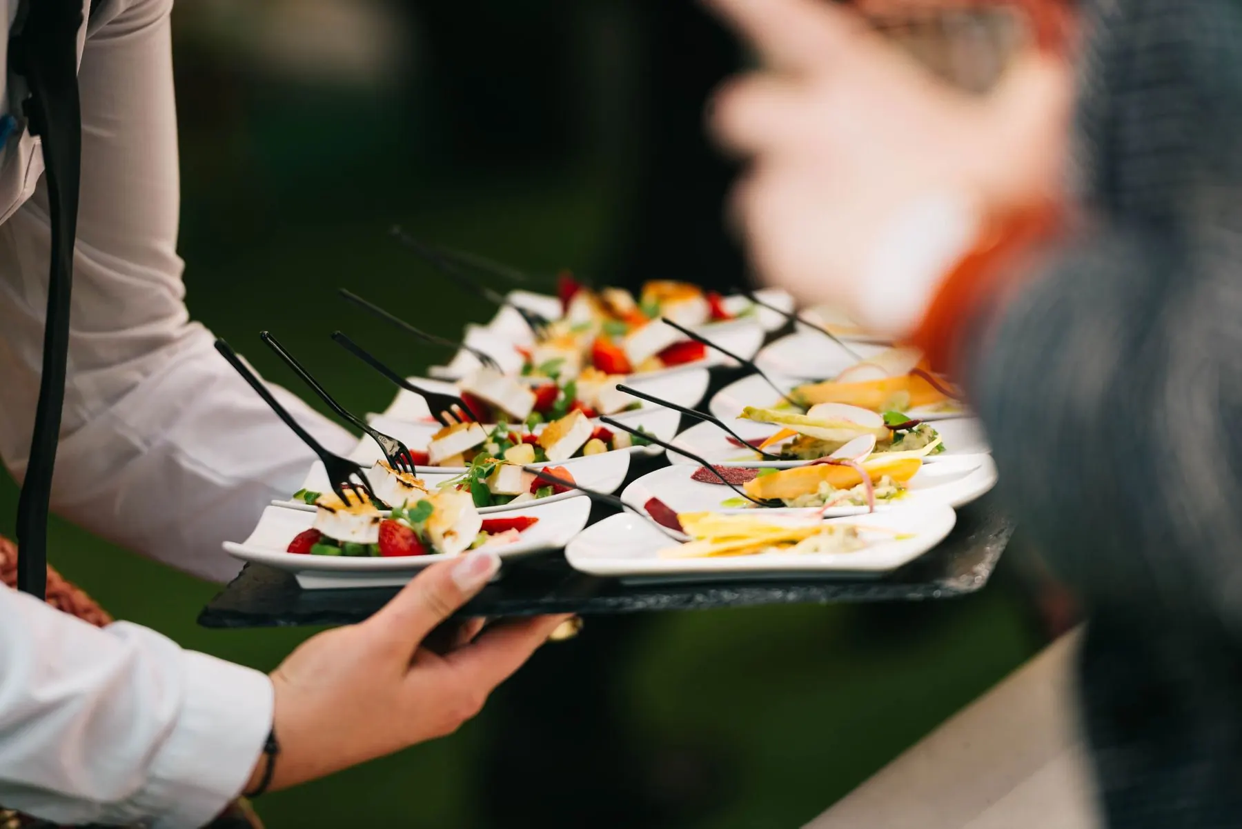Server holding a tray of canapés and mini burgers at an event